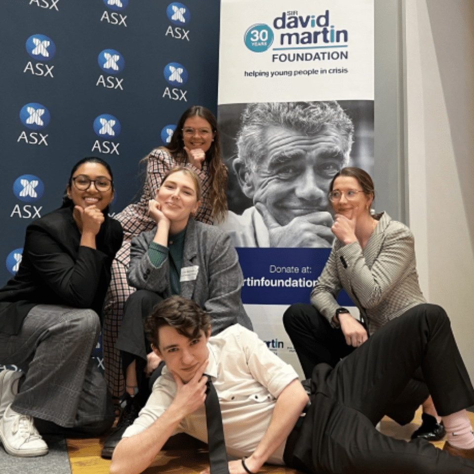 Youth Advisory Group kneeling and smiling in front of a banner of Sir David Martin