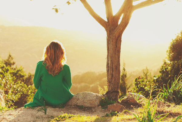 Young woman sitting under a tree and looking out at a valley