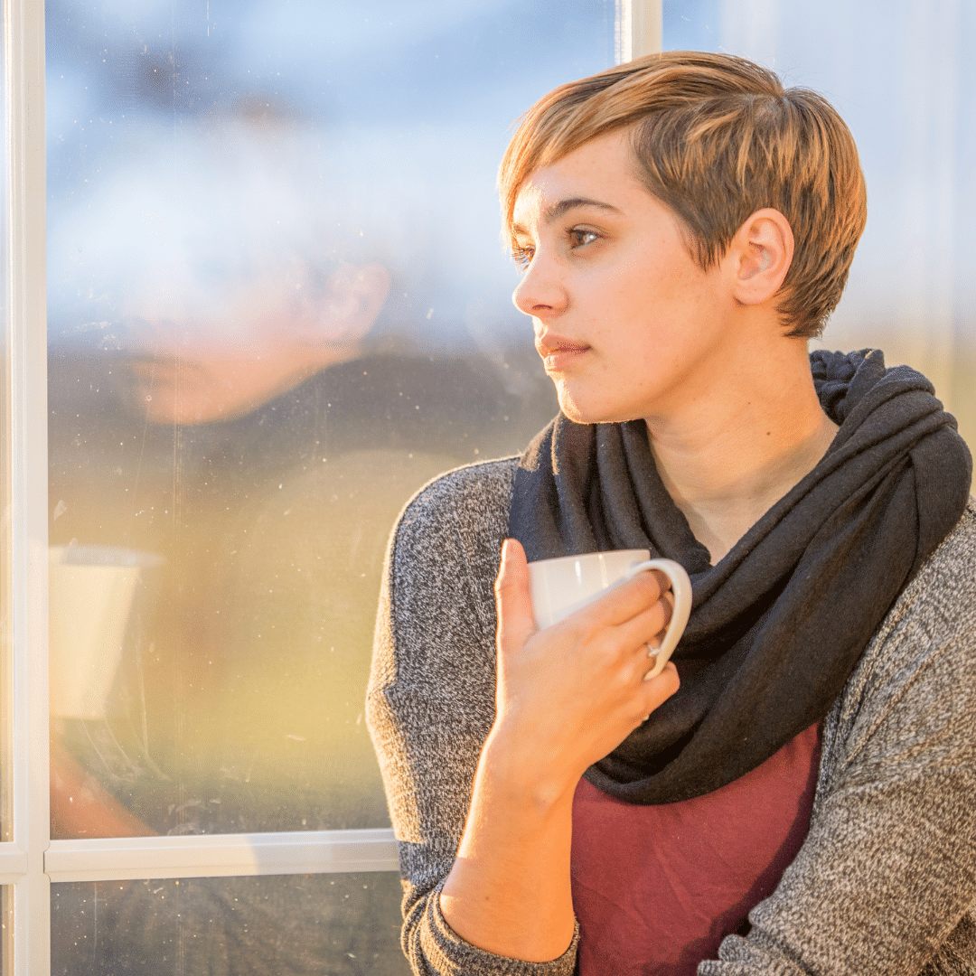 Young woman holding a cup of tea and staring out of a window