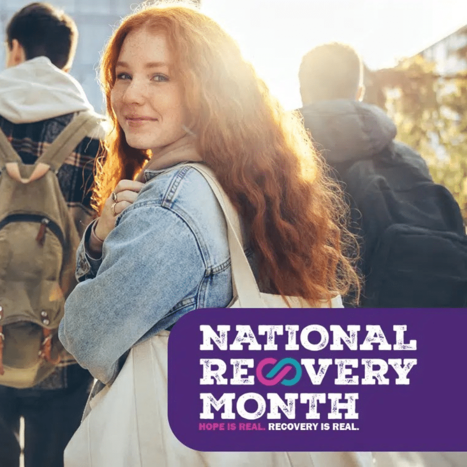 Young woman smiles at the camera behind the National Recovery Month logo