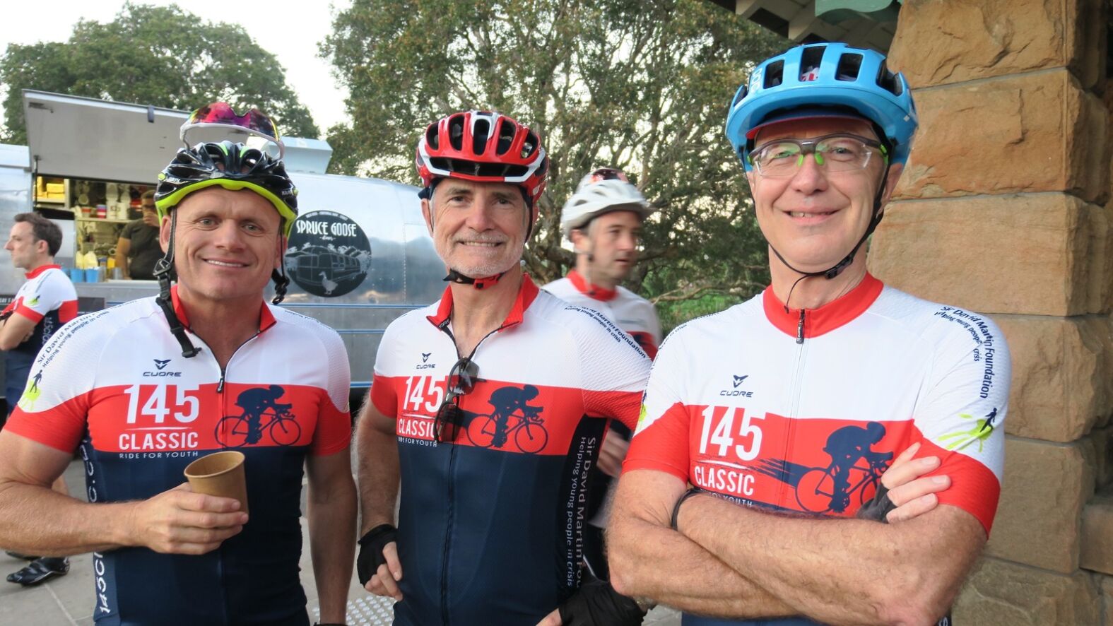Three men in cycling uniforms and helmets smiling