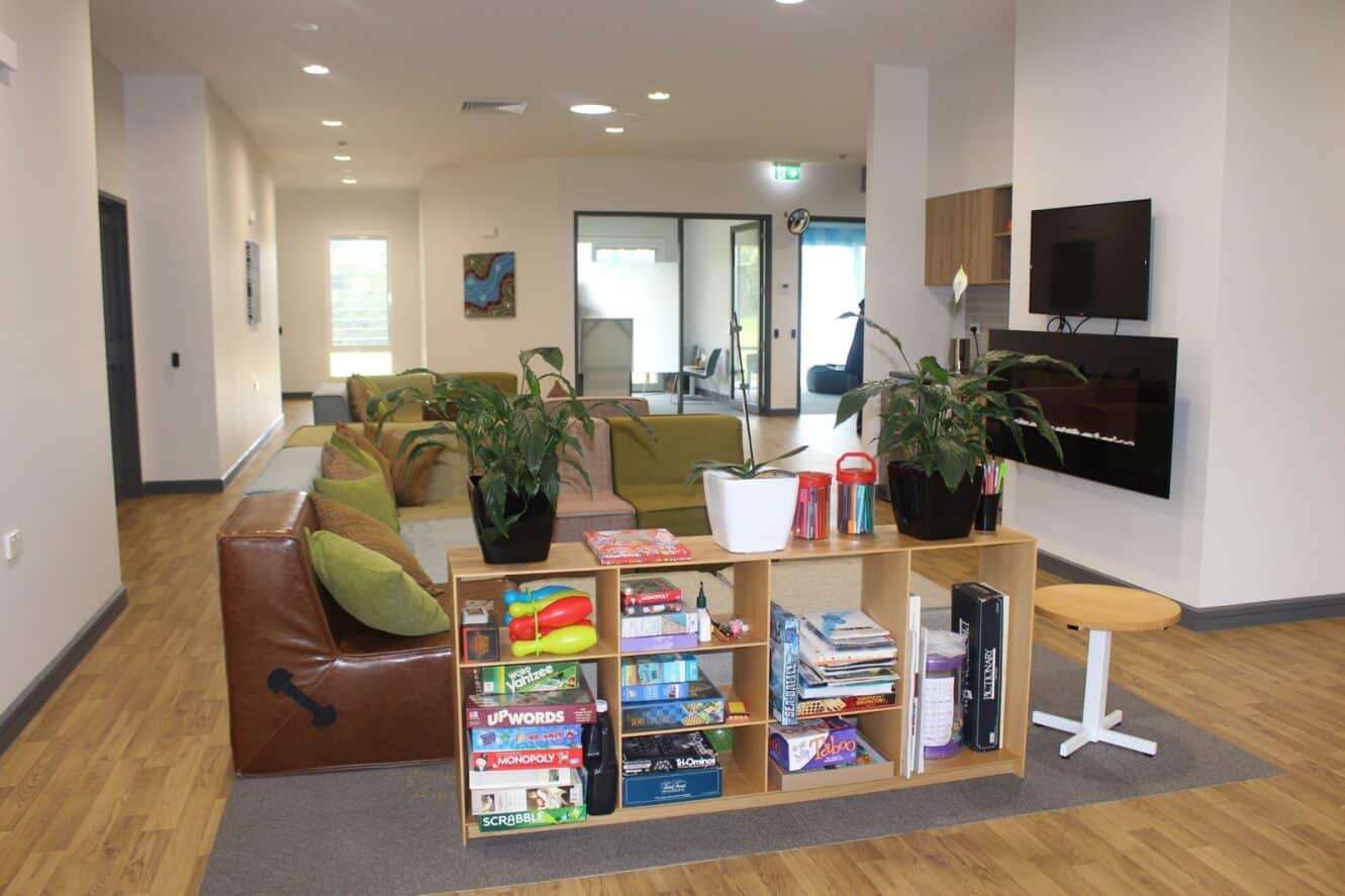 The living area at David Martin Place with a sofa, bookshelf full of board games, and TV.
