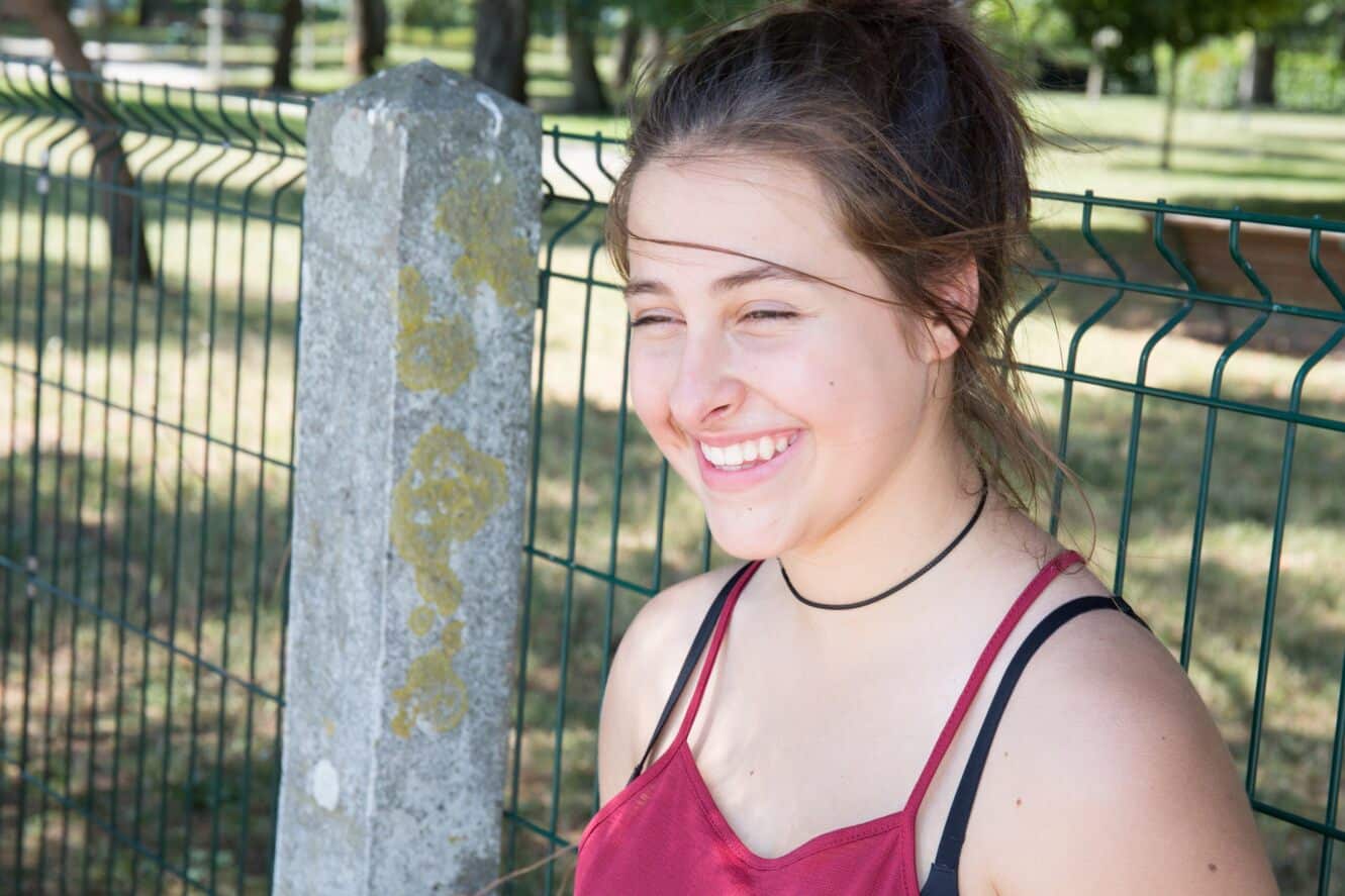 young woman leaning against a fence outside and smiling