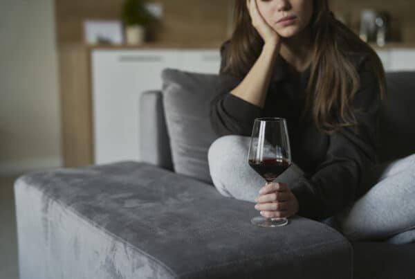 young woman sits sadly holding a glass of wine