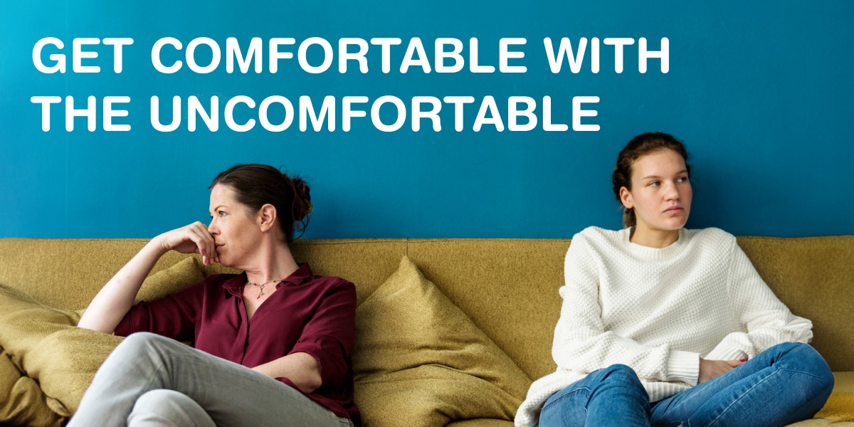 Two people sitting awkwardly on a couch. Text says 'Get comfortable with the uncomfortable'.