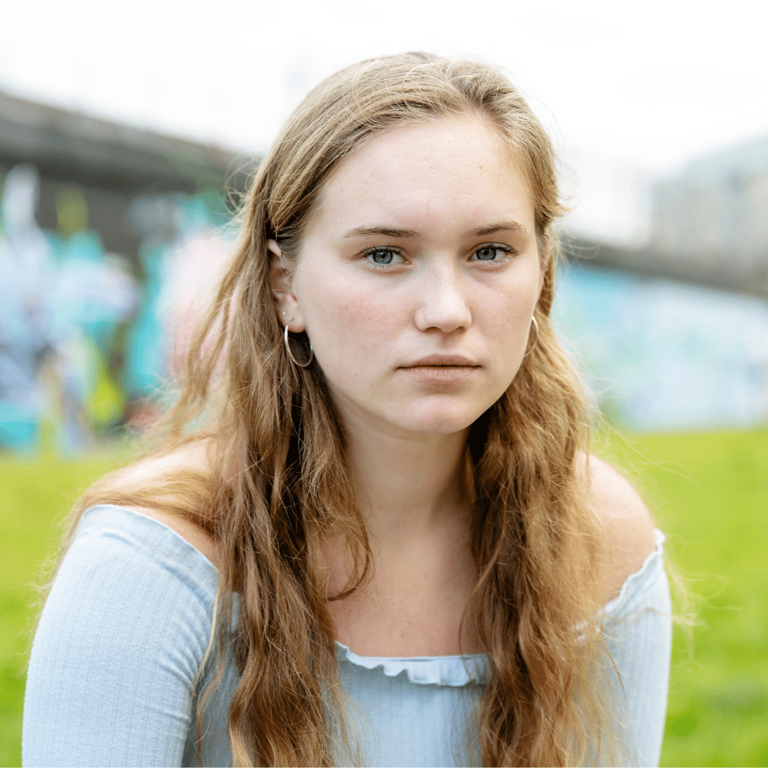 young woman sitting outside and looking seriously towards the camera