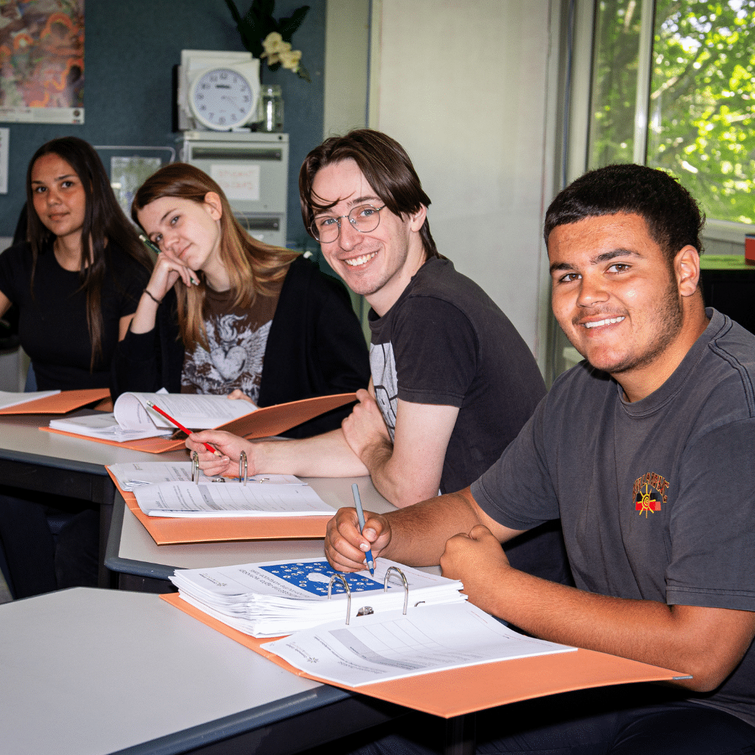 A group of young people sitting in a classroom at Triple Care Farm with pens and paper, smiling