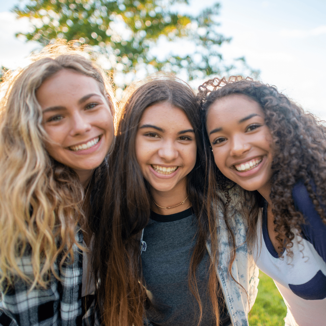 Three young women outside, smiling together