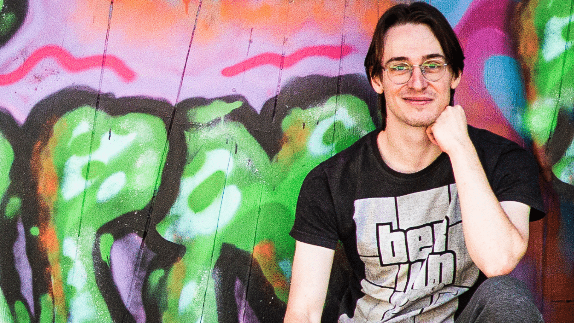 young man in front of a graffiti wall, looking confidently at the camera