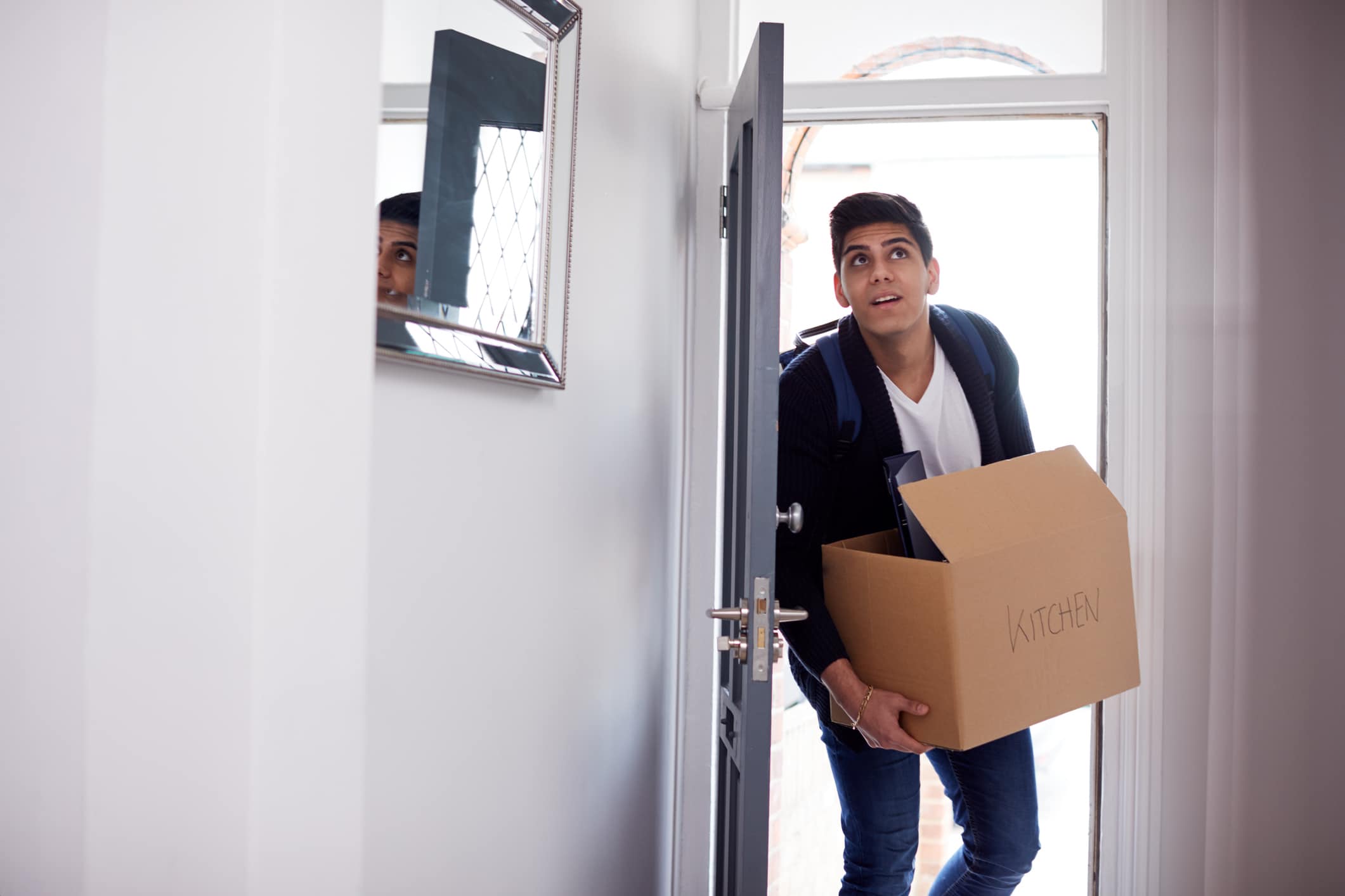 Young man walking into a house holding a cardboard box