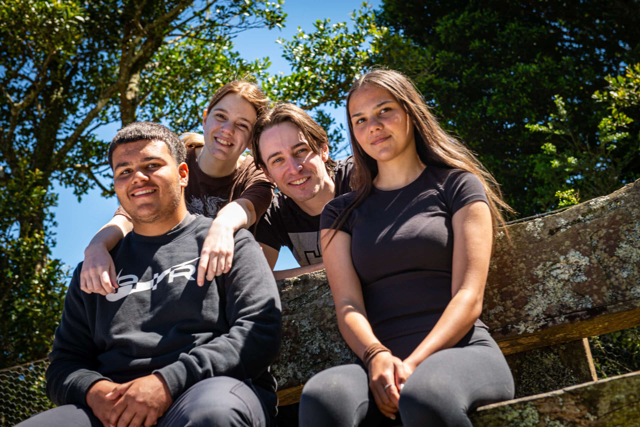 A group of young people sitting outside on a bench and smiling