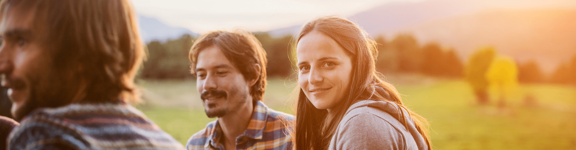 Group of young people sitting outside in a field and smiling.