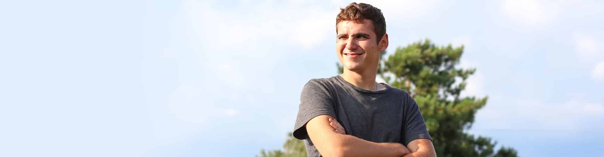 Young man standing outside on a sunny day and smiling proudly, arms folded