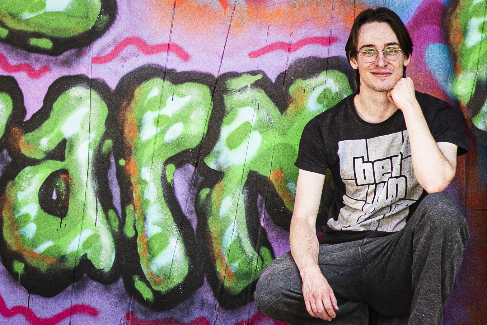 Young man looking confident, kneeling against a colourful gaffiti wall