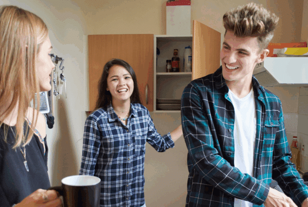 Three young people in an apartment kitchen, chatting and washing the dishes