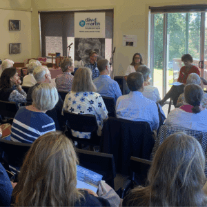 A large room at Triple Care Farm full of people sitting in rows, watching a panel event at the front of the room. The audience's backs are to the camera.