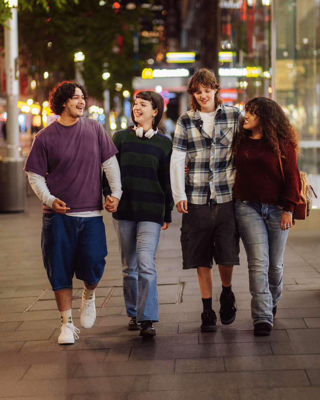 Four happy teens walk through the city at night.
